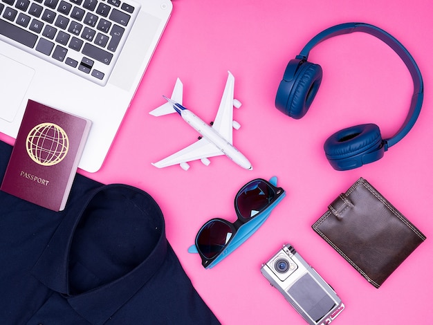 Vista dall'alto piatta degli accessori del fotografo viaggiatore su sfondo rosa. passaporto. il computer portatile. cuffie. portafoglio . occhiali da sole