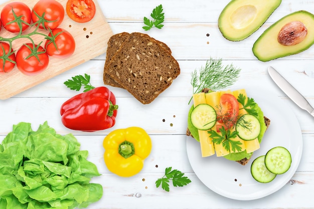 Vista dall'alto piatto di colazione sana ed energica pane scuro pomodori avocado peperoni cetriolo e panino vegetale con formaggio su un tavolo in legno vintage