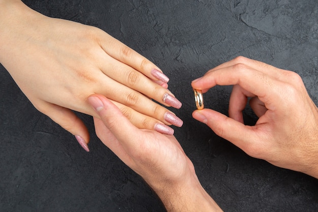 vista dall'alto proposta di matrimonio concetto mani dell'uomo posizionando l'anello nuziale sulla mano della donna su sfondo scuro