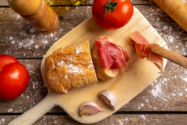 vista dall'alto prosciutto, pane e pomodori sulla tavola di legno