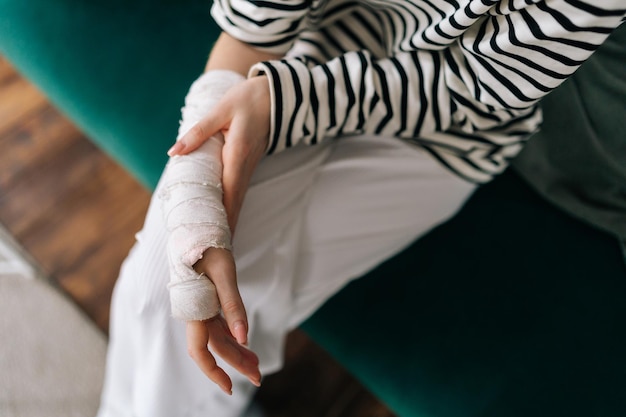 Vista dall'alto ritagliata di una giovane donna irriconoscibile con la mano destra rotta avvolta in una benda di gesso bianco che massaggia delicatamente il braccio ferito