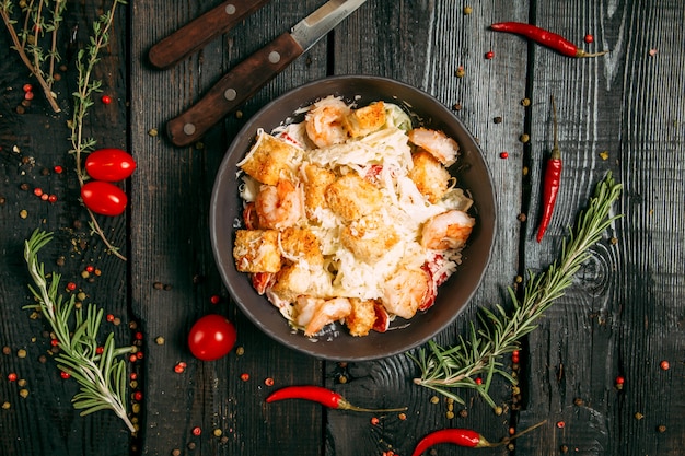 Vista dall'alto su caesar salad fresco di verdure, pollo e formaggio in una ciotola scura sullo sfondo in legno scuro