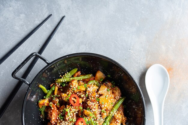 Vista dall'alto sul pad thai, o phad thai in padella di pasta di riso con verdure e pollo, peperoncino piccante e prezzemolo in ciotola nera sulla superficie di pietra grigia