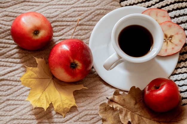 Vista dall'alto sulla tazza di caffè espresso su plaid circostante con foglie autunnali ingiallite e mele rosse