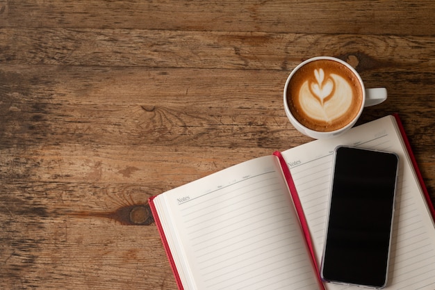 Vista dall&#39;alto Taccuino con matita, smart-phone e una tazza di caffè sul tavolo di legno per sfondo di affari