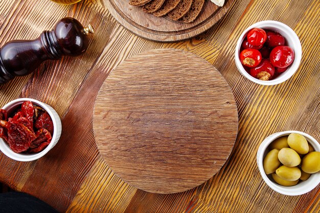 Vista dall'alto tagliere vuoto per pizza o carne. Scheda in bianco per servire cibo in composizione con, pomodori secchi, bruschetta e utensili su fondo di legno. Disteso