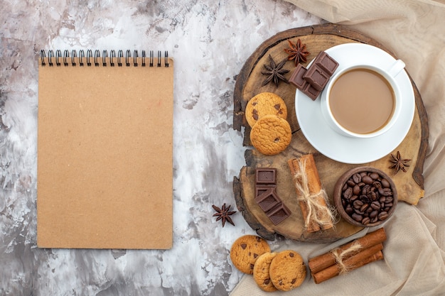 vista dall'alto tazza di caffè biscotti ciotola con chicchi di caffè tostato cioccolato bastoncini di cannella legati con corda anice su tavola di legno taccuino sul tavolo