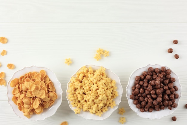 Vista dall'alto tre diversi cereali per la colazione su una ciotola bianca, palline di cioccolato, corn flakes e stella di miele, spazio per copiare il testo
