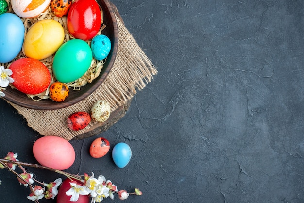 vista dall'alto uova di pasqua colorate all'interno del piatto con paglia su superficie scura