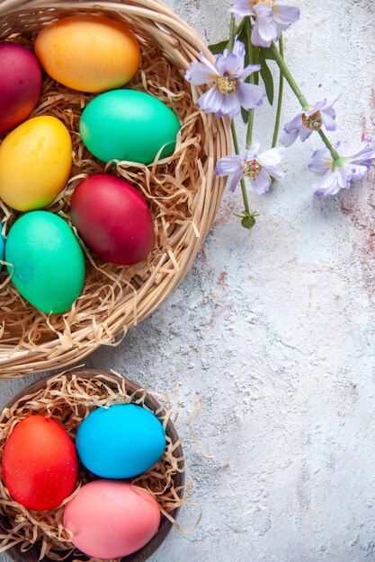 vista dall'alto uova di pasqua colorate all'interno del piatto e del cestino su superficie bianca