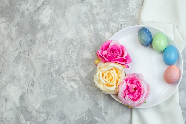 vista dall'alto uova di pasqua colorate con fiori all'interno del piatto su superficie bianca