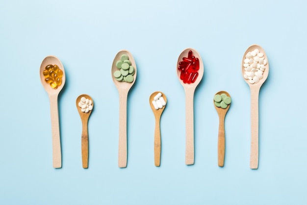 Vista dall'alto Varietà di pillole di vitamine e minerali in cucchiaio di legno su sfondo colorato Vista dall'alto di pillole farmaceutiche assortite Prodotto sanitario integratore alimentare