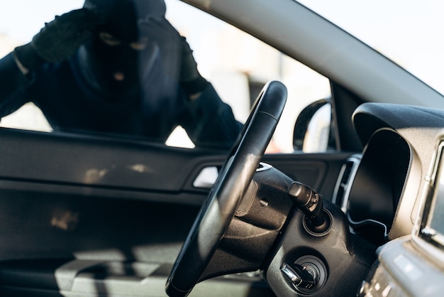 Vista dall'auto all'uomo vestito di nero con un passamontagna in testa che guarda il vetro dell'auto prima del furto. Ladro d'auto, concetto di furto d'auto