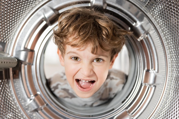 Vista dall'interno della lavatrice Un ragazzo con i capelli ricci mette la testa dentro il cestello fa una faccia stupida scioccata con gli occhi spalancati e il viso