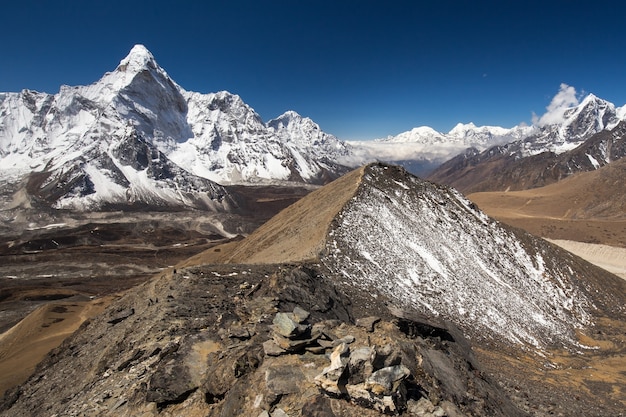 Vista dalla cima di una collina con un pendio innevato del Monte Ama Dablam innevato panorama in Himalaya con un luminoso cielo blu sopra e un ghiacciaio al di sotto