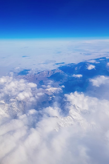 Vista dalla finestra dell'aereo al cielo blu e cime innevate in nuvole bianche