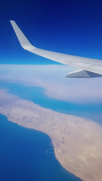 Vista dalla finestra dell'aereo su cielo blu e terra con paesaggio di mare deserto e canali negli Emirati