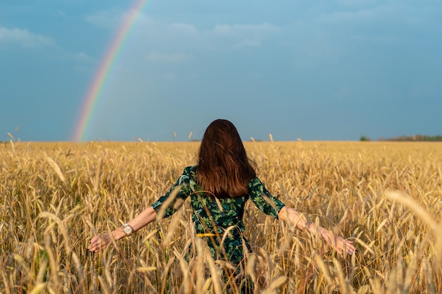 Vista dalla parte posteriore di una giovane donna in un campo con le mani di grano ai lati delle orecchie