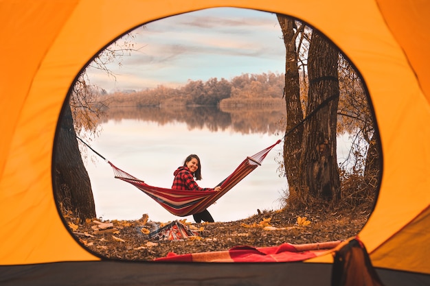 Vista dalla tenda donna seduta sull'amaca con il lago sullo sfondo autunno stagione autunnale