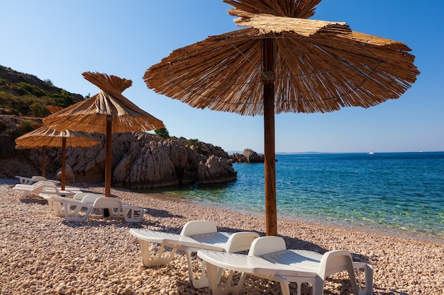 Vista degli ombrelloni di paglia nella bellissima spiaggia di Oprna nella baia adriatica dell'isola di Krk, in Croazia