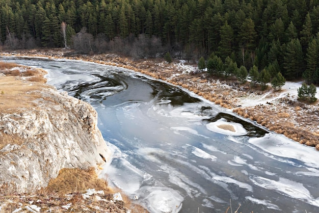 Vista del fiume coperto dalle prime scogliere di neve ghiacciata con foresta di erba beige secca in autunno o in inverno