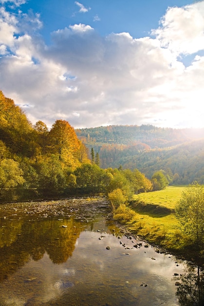 Vista del paesaggio idilliaco del fiume quando il sole sta per tramontare sulla collina in una colorata foto verticale di una giornata autunnale