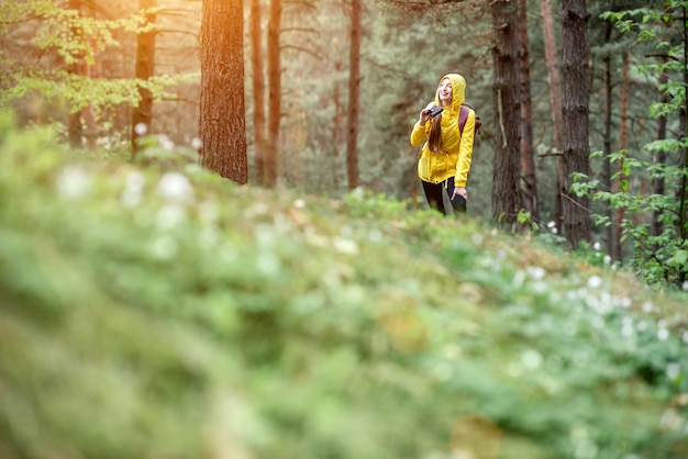 Vista del paesaggio sulla foresta di pini con la donna che fa un'escursione in impermeabile giallo