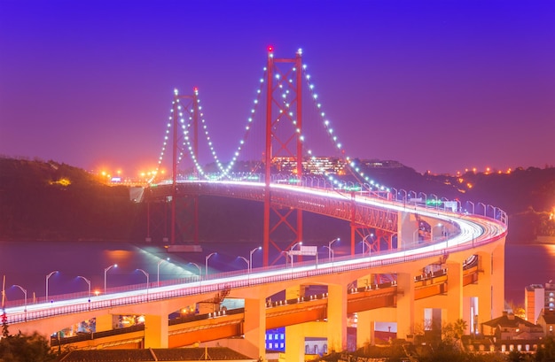 Vista del ponte 25 aprile (Ponte 25 de Abril) con percorsi di luce auto nella foschia. Punto di riferimento popolare di Lisbona, Portogallo