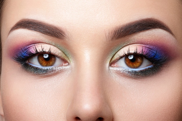 Vista del primo piano degli occhi femminili marroni con trucco smokey eyes rosa e blu colorato