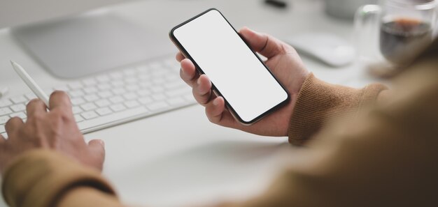 Vista del primo piano del giovane che lavora al suo progetto con lo smartphone dello schermo in bianco