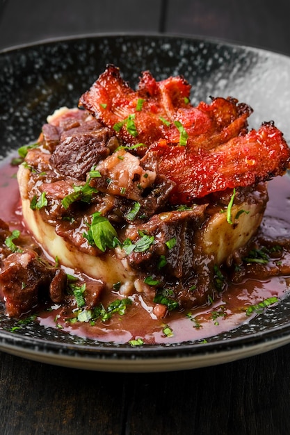 Vista del primo piano del gulasch di manzo con patatine di pancetta, purè di patate e salsa di ribes nero su un piatto