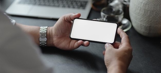 Vista del primo piano dell'uomo d'affari che tiene lo smartphone dello schermo in bianco nella sua stanza moderna dell'ufficio