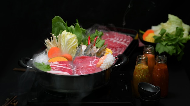 Vista del primo piano dello shabu di shabu in pentola calda con fondo nero, carne affettata fresca, frutti di mare e verdure