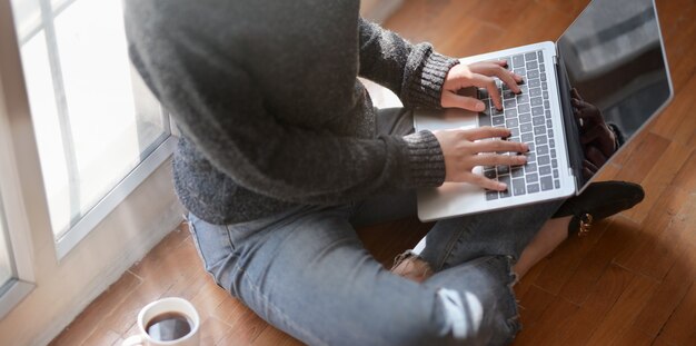 Vista del primo piano di giovani free lance femminili che scrivono sul computer portatile mentre sedendosi accanto alle finestre