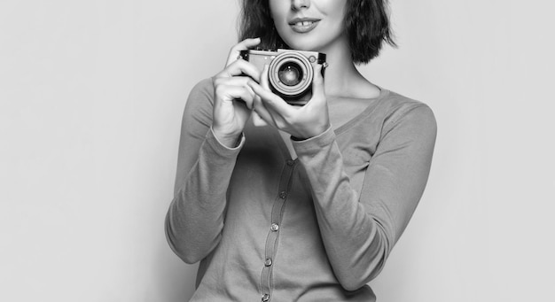 Vista del raccolto del fotografo della donna che tiene la macchina fotografica della foto nelle mani di fondo beige che fotografa