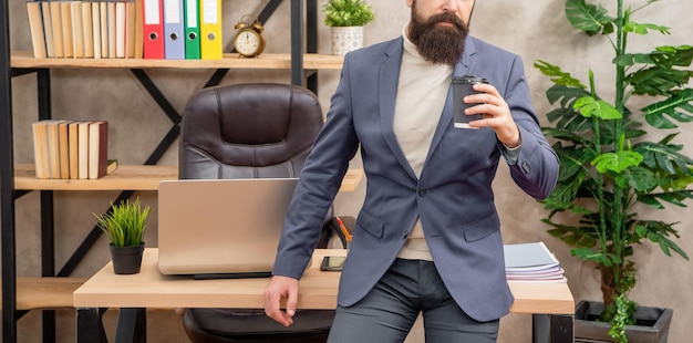 Vista del raccolto professionale del ragazzo che beve tè o caffè seduto sulla pausa della scrivania dell'ufficio