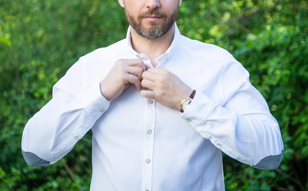 Vista del raccolto professionale del ragazzo con la barba lunga che si abbottona la camicia sullo sfondo naturale