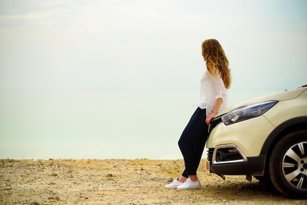 Vista del viaggiatore della giovane donna che esamina tramonto del mare, sedentesi sulla automobile della berlina