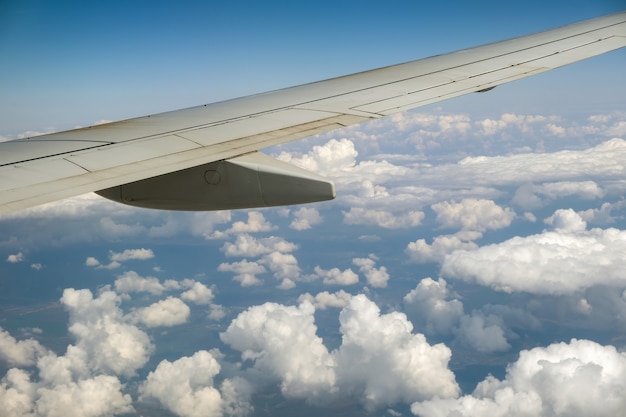 Vista dell'ala dell'aereo a reazione dall'interno che sorvola le nuvole gonfie bianche nel cielo blu. Concetto di viaggio e trasporto aereo.
