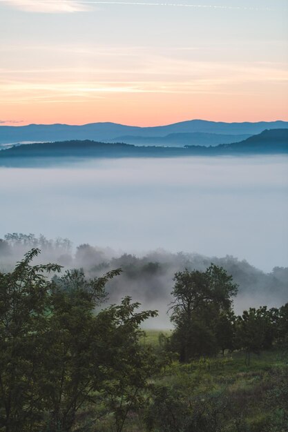 Vista dell'alba sulle montagne, nebbia e nuvole sotto le cime