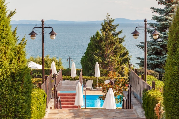 Vista dell'area ricreativa dell'hotel con ombrelloni e lanterne in piscina sullo sfondo di alberi e mare