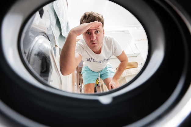 Vista dell'uomo dalla lavatrice all'interno L'uomo fa il bucato routine quotidiana Mano sulla fronte che guarda lontano guardando o cercando