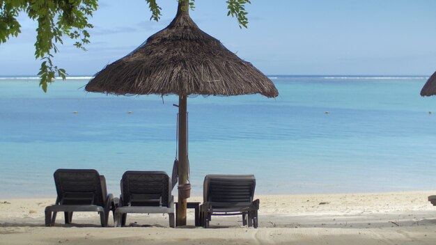 Vista della chaiselongue vuota vicino all'ombrellone nativo contro l'isola mauritius dell'acqua blu