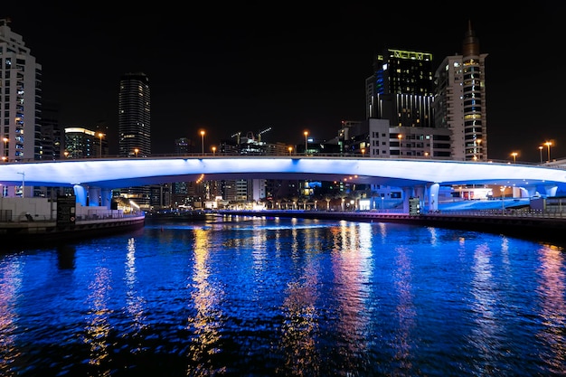 Vista della passerella con i turisti che portano a numerosi grattacieli con hotel ed edifici residenziali sulla costa del Golfo Persico a Dubai di notte