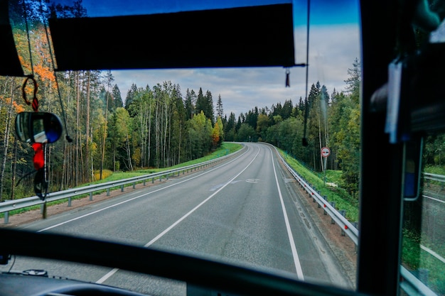 Vista della strada e della foresta autunnale attraverso il viaggio su strada del finestrino dell'autobus