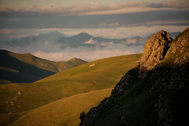 Vista delle colline ricoperte di erba verde in primo piano di alta collina rocciosa