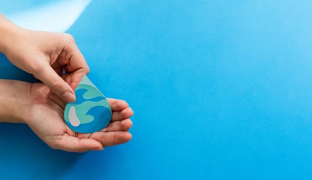 Vista delle mani della donna che tengono carta tagliata goccia d'acqua su sfondo blu - Giornata mondiale dell'acqua