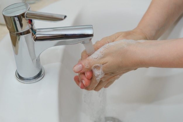 Vista delle mani femminili in schiuma saponosa sotto il primo piano dell'acqua di rubinetto