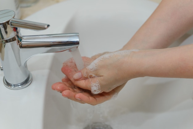 Vista delle mani femminili in schiuma saponosa sotto il primo piano dell'acqua di rubinetto