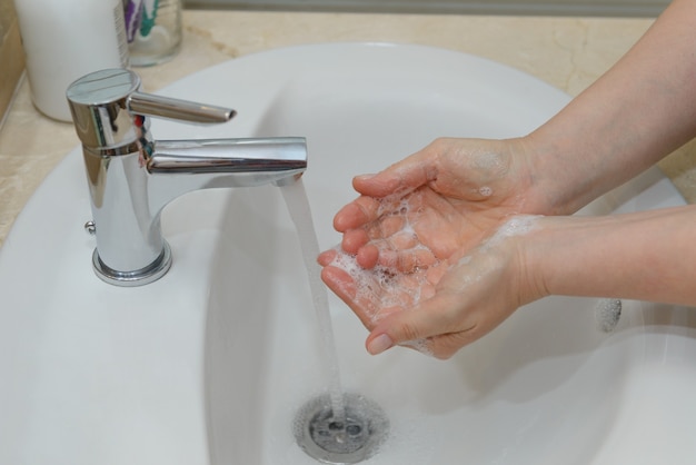 Vista delle mani femminili in schiuma saponosa sotto il primo piano dell'acqua di rubinetto